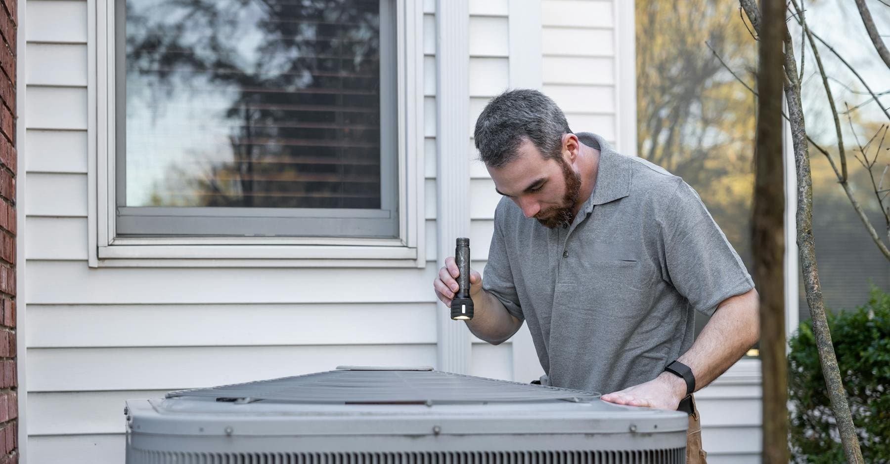 Technician inspecting an outdoor air conditioning condenser